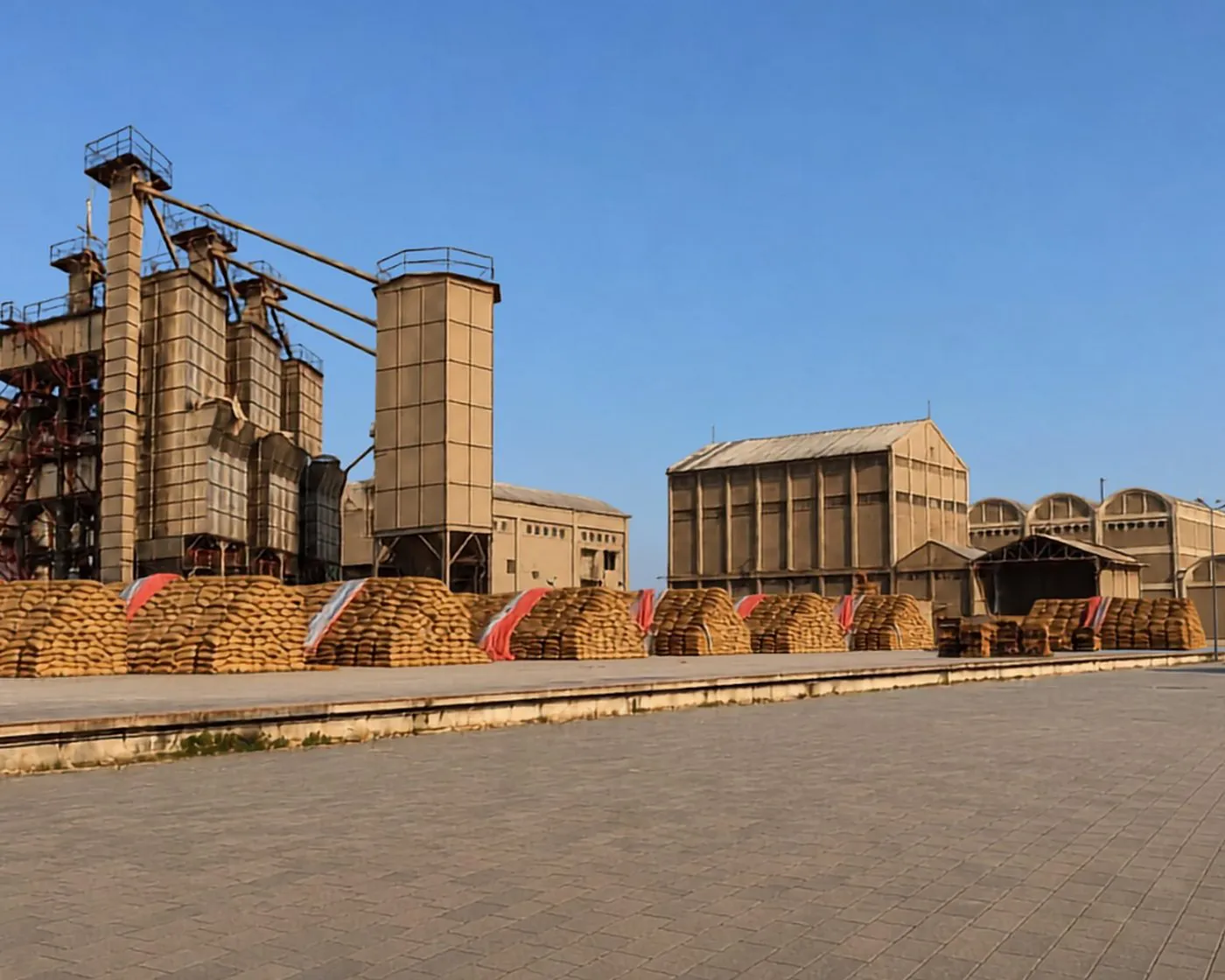 Paddy silos beside stacked jute bags in the yard of a Green International Rice mill
